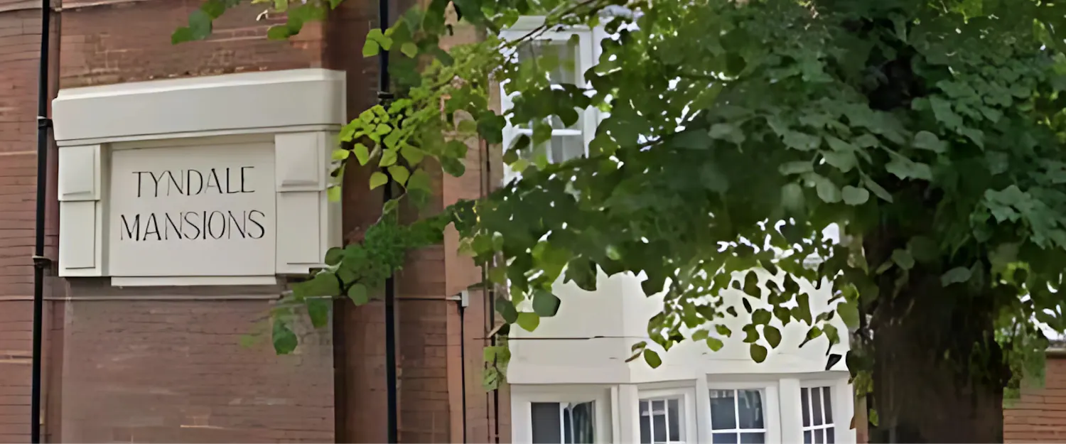 Close up of Tyndale Mansions sign on side of building with tree in the foreground