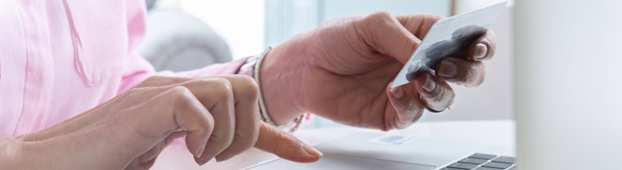 Image of persons hands.  One hand is typing on a laptop and the other is holding a bank card.