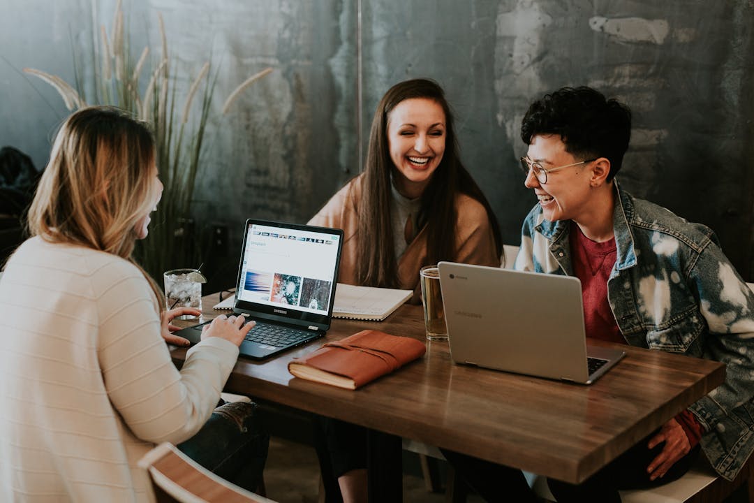 Three people laughing sitting at a table with laptops