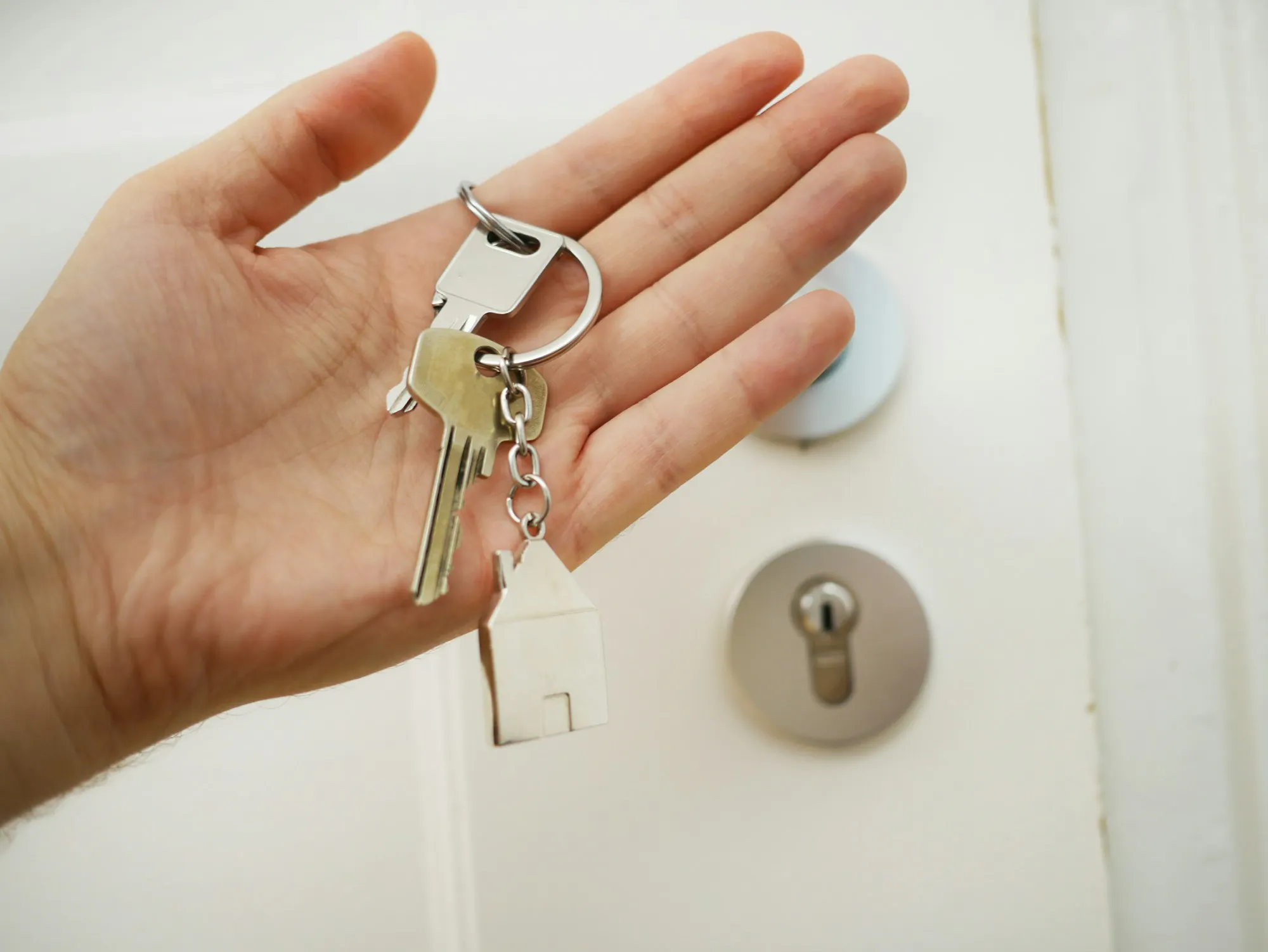 Open palm holding a set of house keys in front of a door