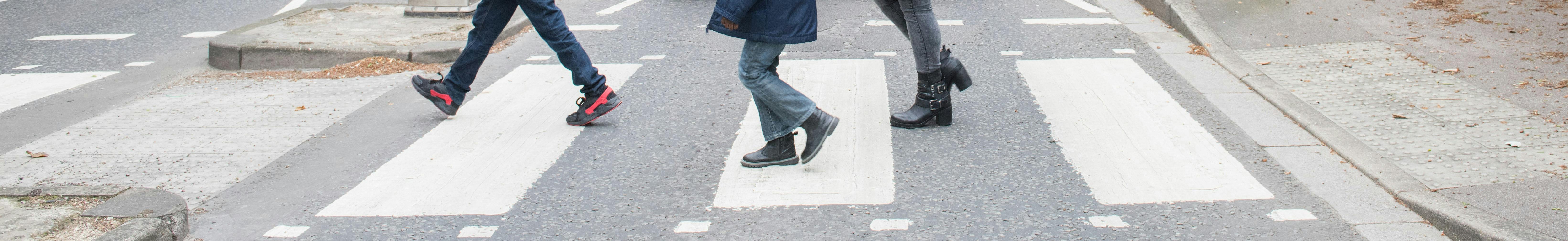 View of a Zebra Crossing with the feet of a mother and two sons crossing the road 