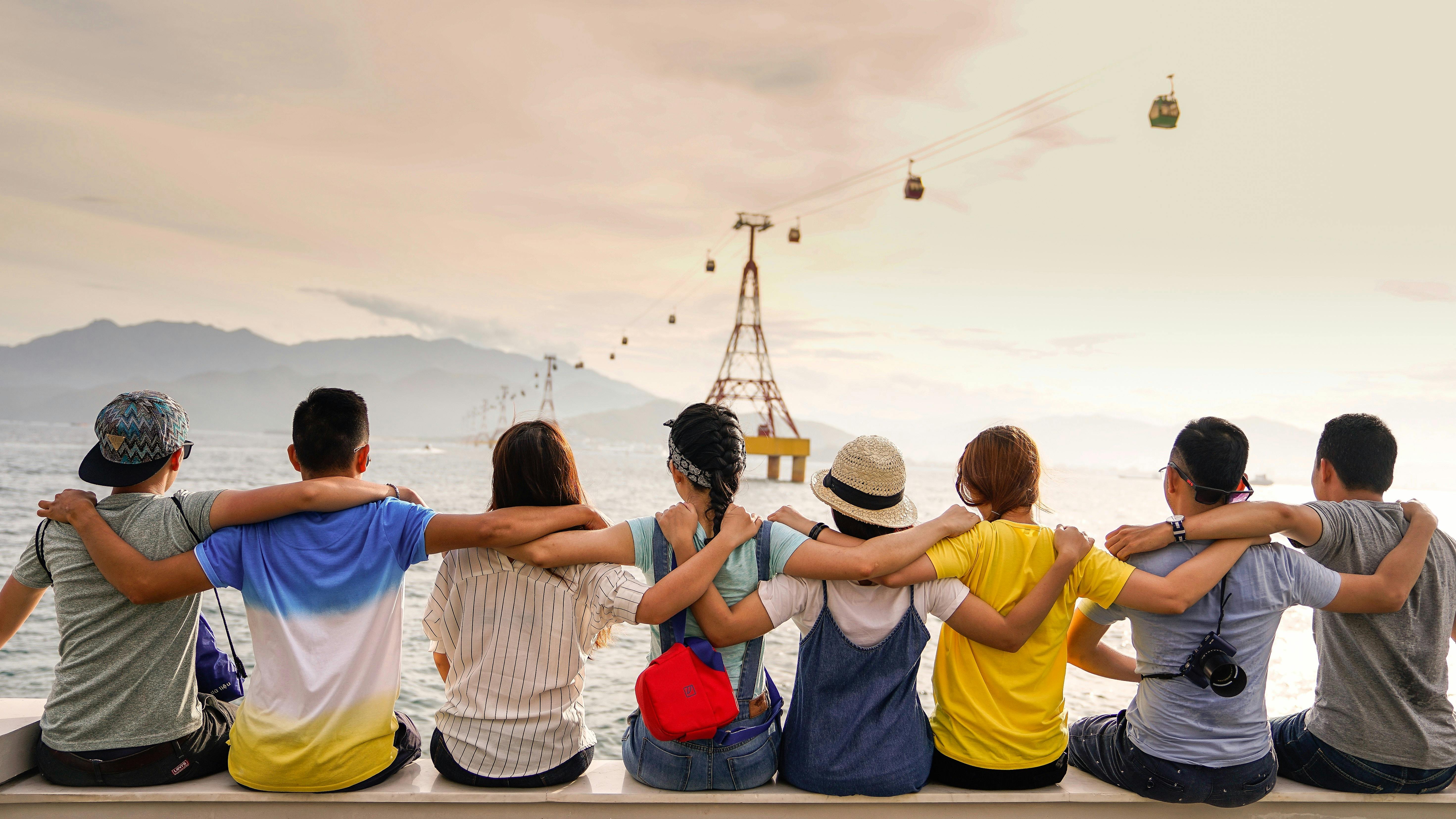 A group of 8 teenagers sitting arm in arm looking out to sea