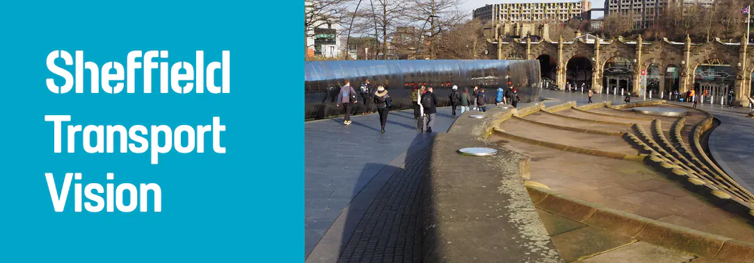 People walk down a slope toward Sheffield train station, the station and trees and a grey sky are in the background