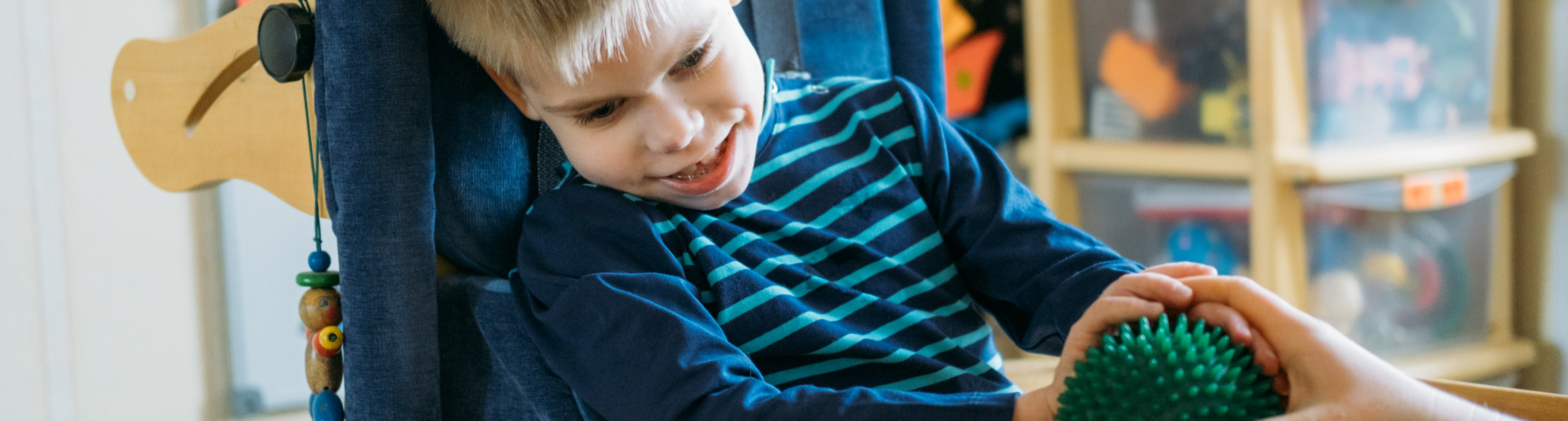 Image of smiling disabled child in wheelchair playing with spiky ball.
