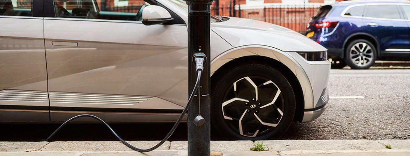 Lamp column electric vehicle charging point next to a parked car plugged in to the charging point.