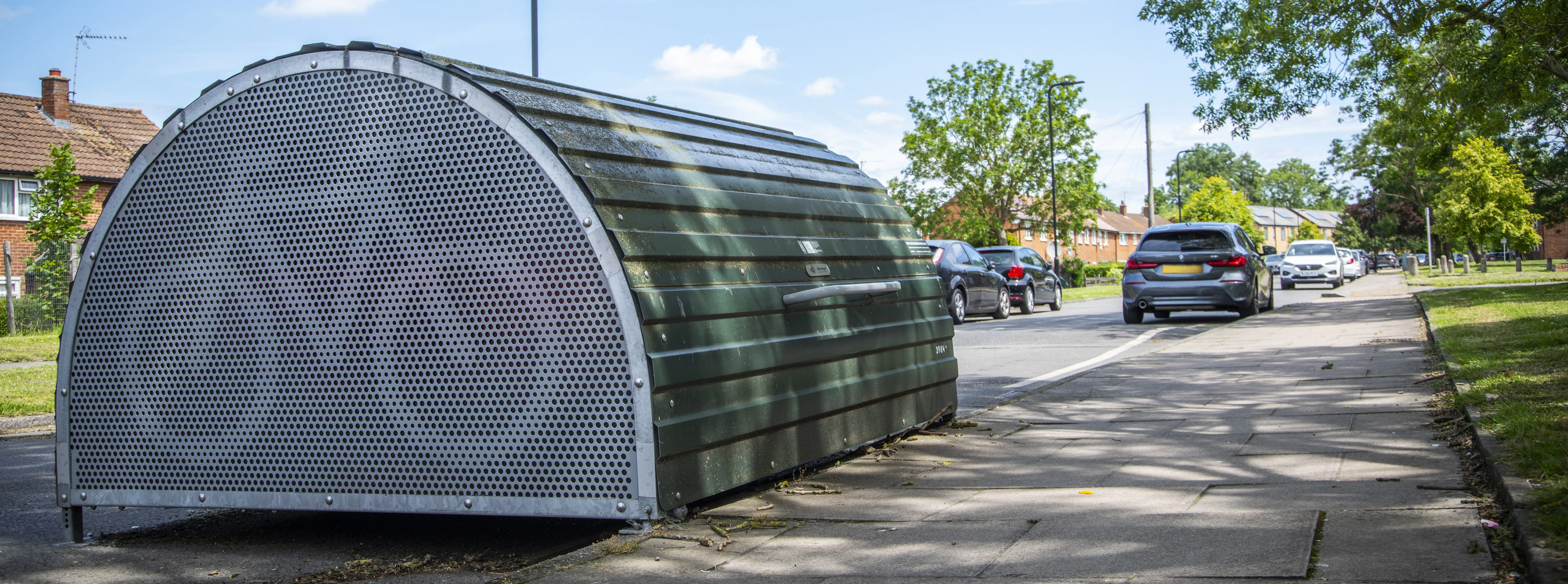 Image of a street in Harrow with a cycle hangar and parked cars 