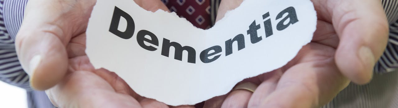 Hands holding a piece of paper with the word Dementia written on it.