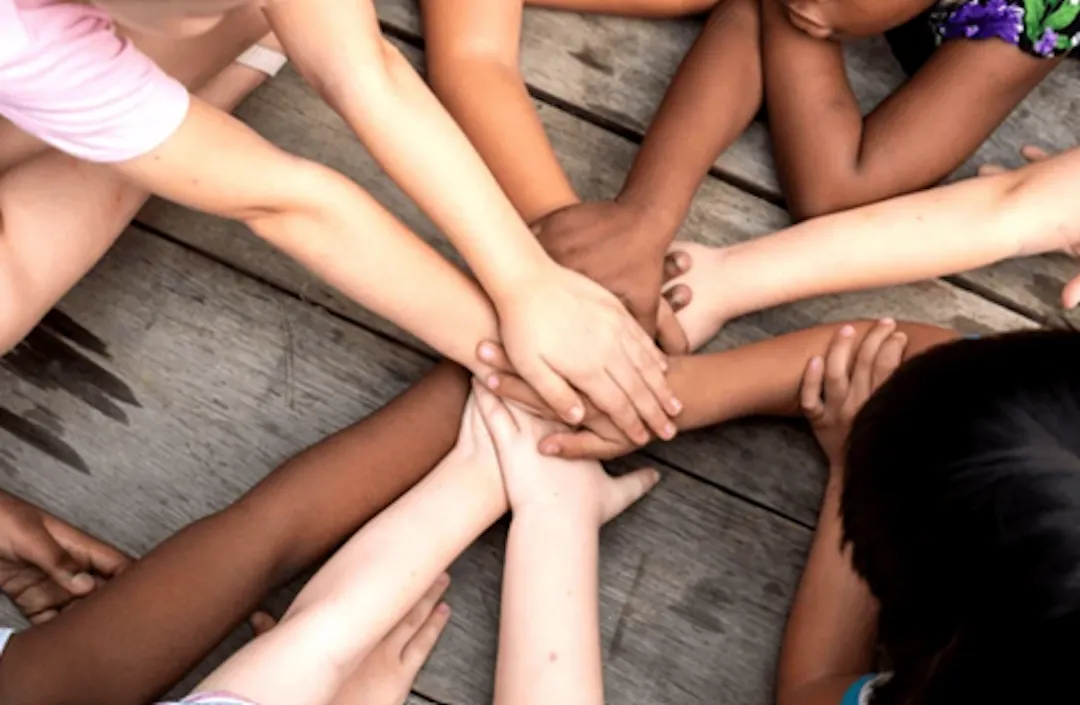 Children joining hands in the centre of a table