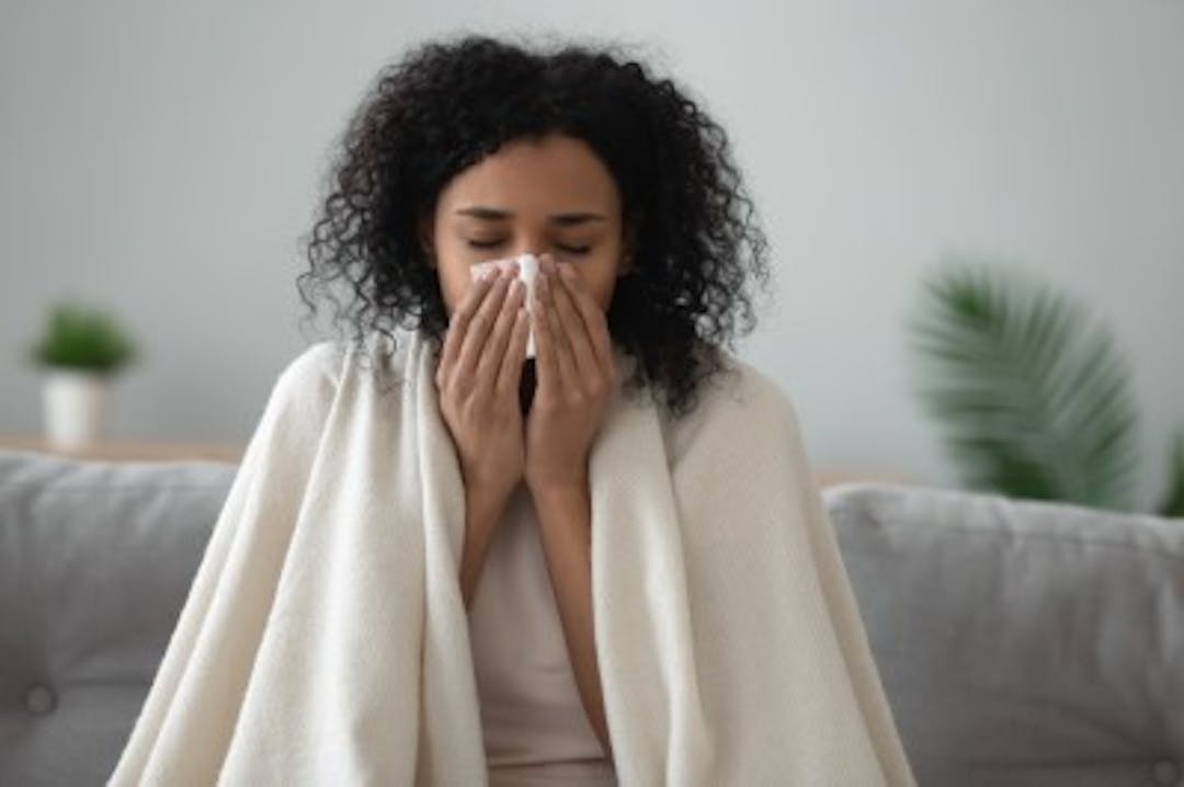 Image of women with blanket wrapped around her shoulders and holder a tissue to her nose with both hands