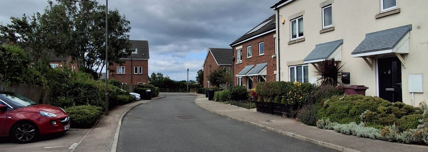 A row of houses with small gardens at the front and parking opposite