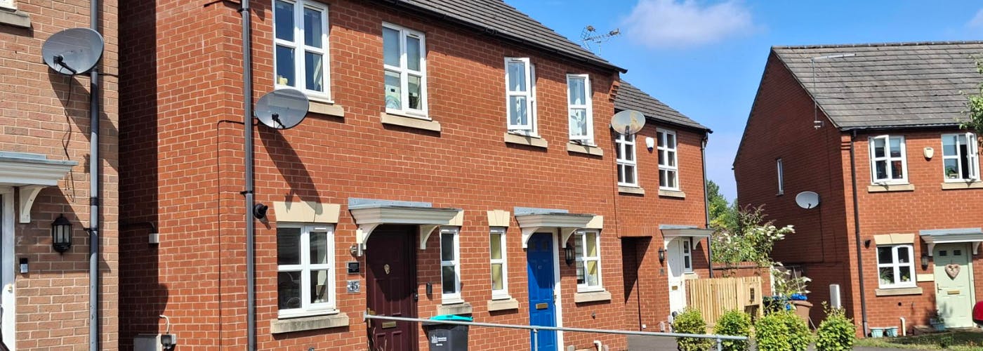 A street of terraced and semi-detached homes in the sunshine with gardens at the front