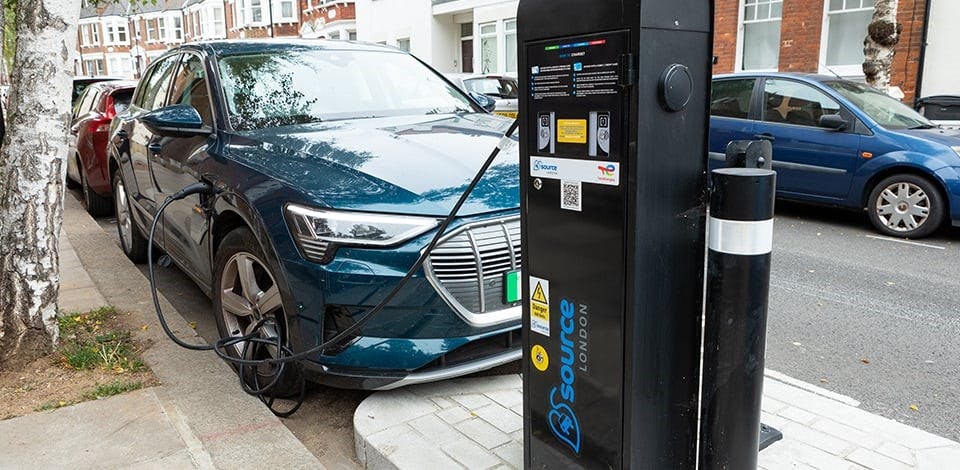 Lamp column electric vehicle charging point next to a parked car plugged in to the charging point.