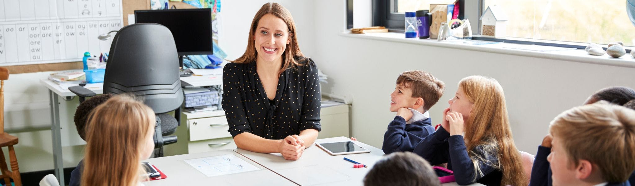 Teacher sitting at a table in a classroom with students