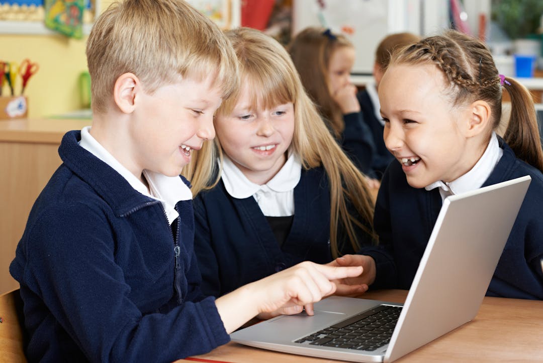 One primary aged male pupil and two female pupils sitting together and working on a shared laptop