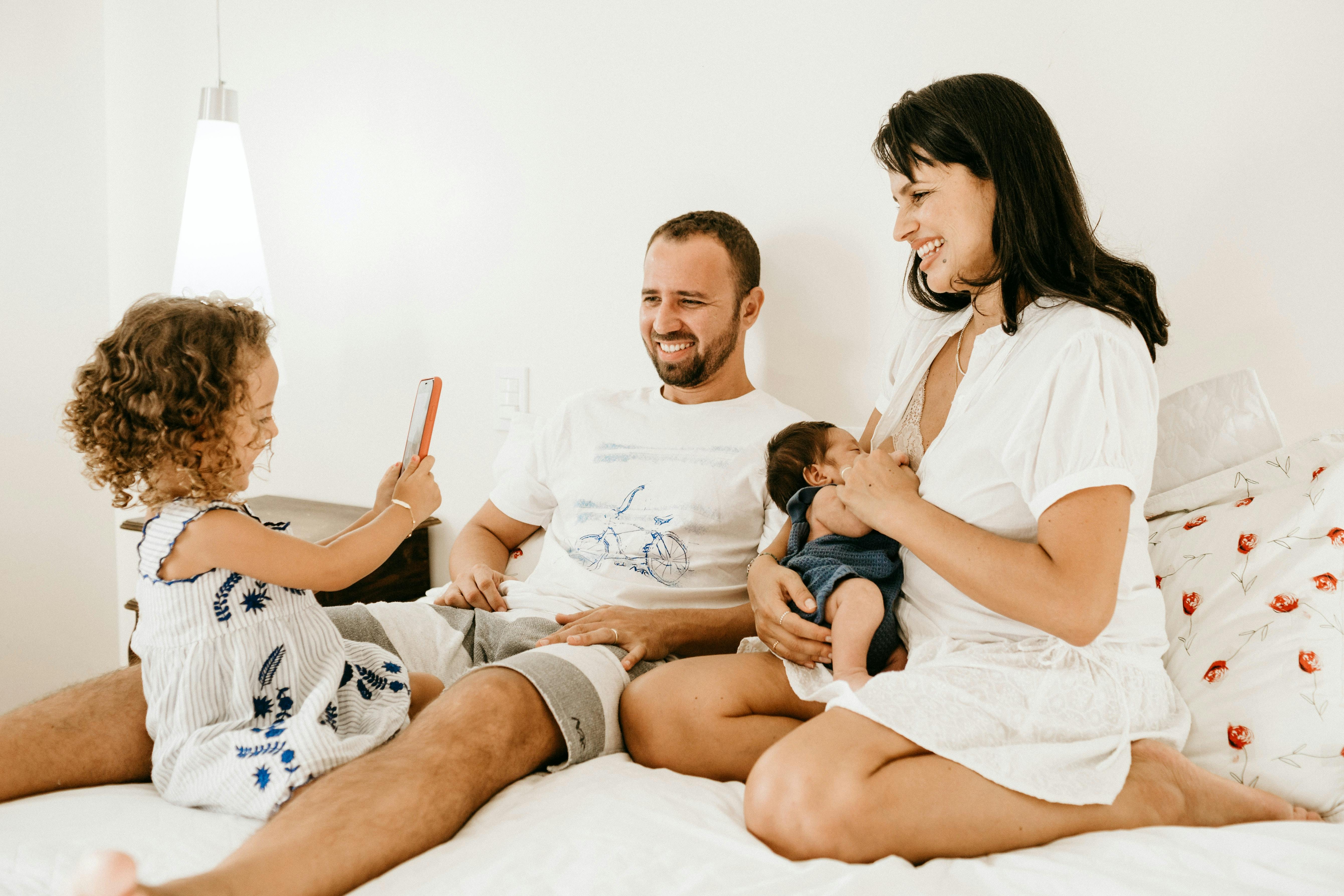 A father, mother, toddler and baby cuddle up on a bed