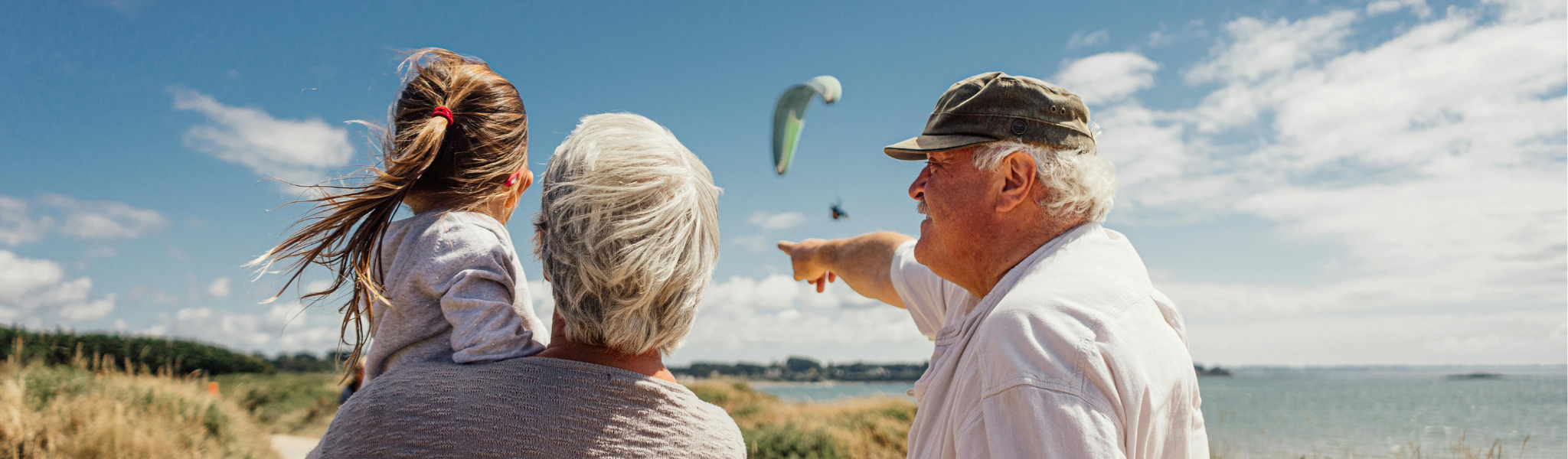 An image of 3 people on a beach looking at a paraglider