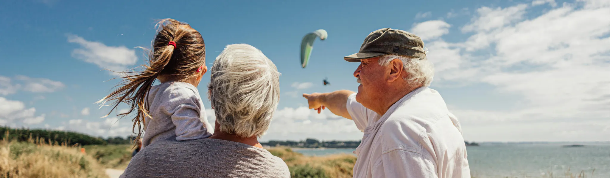 An image of 3 people on a beach looking at a paraglider