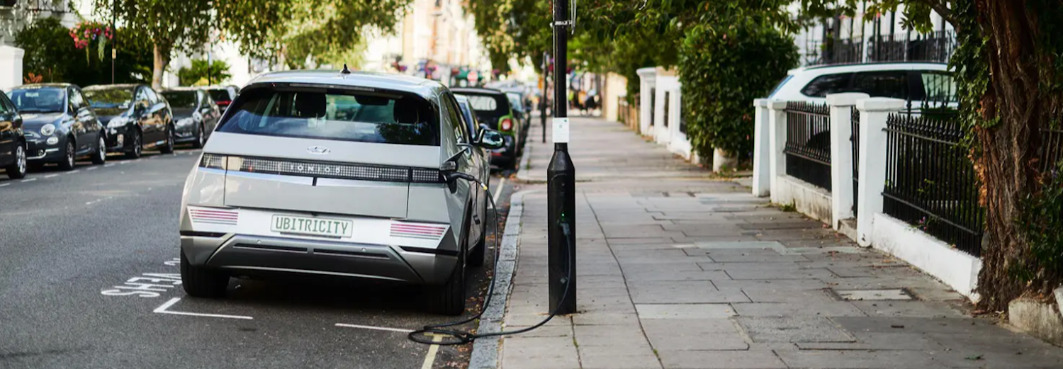 Lamp column electric vehicle charging point next to a parked car plugged in to the charging point.