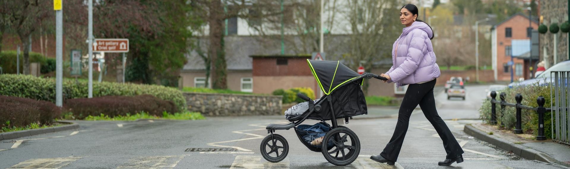 A lady uses a zebra crossing to cross with her pushchair. 