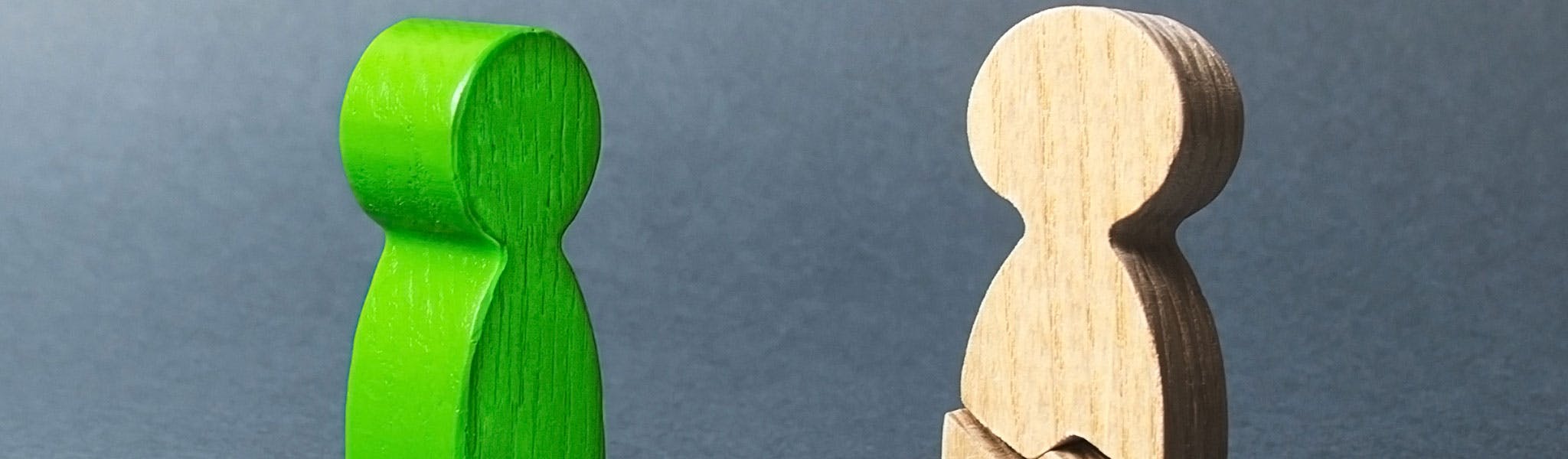 This is an image of two wooden people one green and one broken 