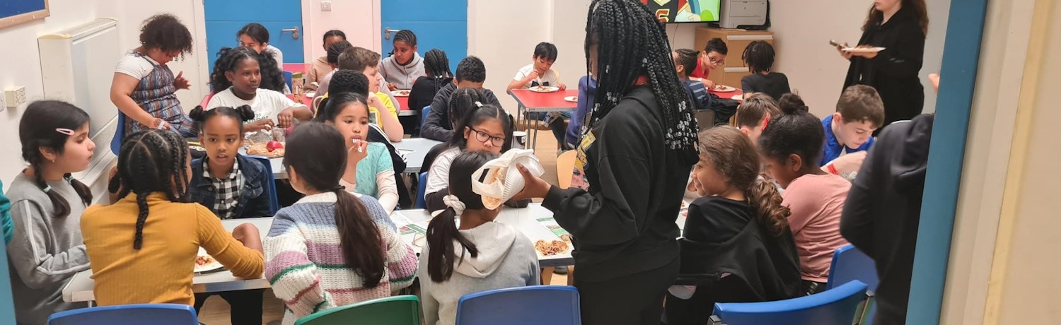 Young children in a classroom eating lunch with two teachers in attendance