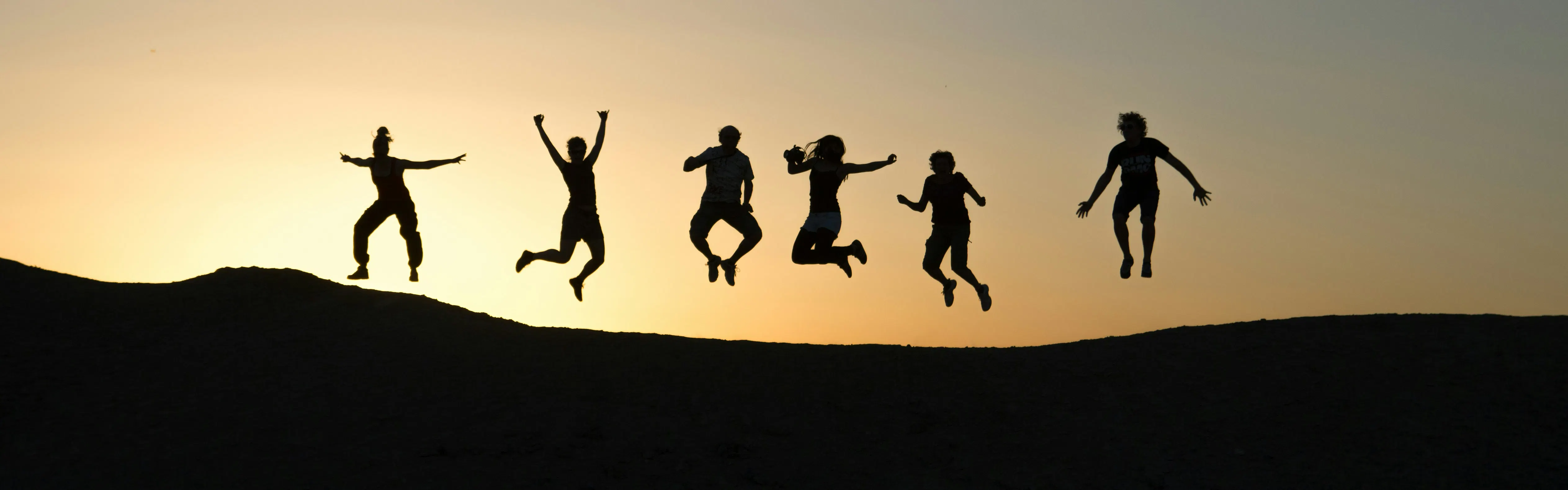 Shadow outline of six people on a hilltop facing the sunset so we can only see thier outlines