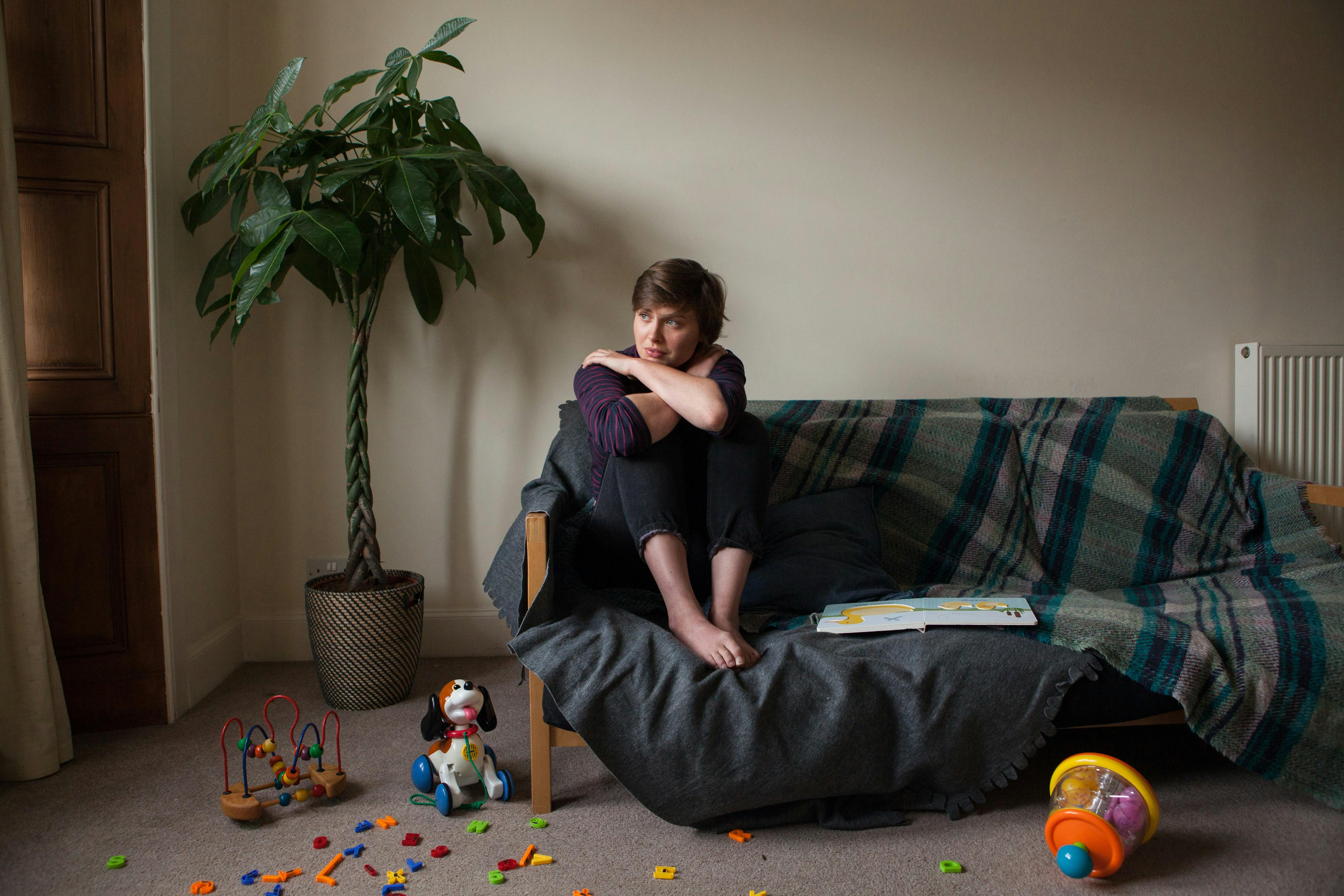 woman sitting on a sofa with children's toys scattered on the carpet