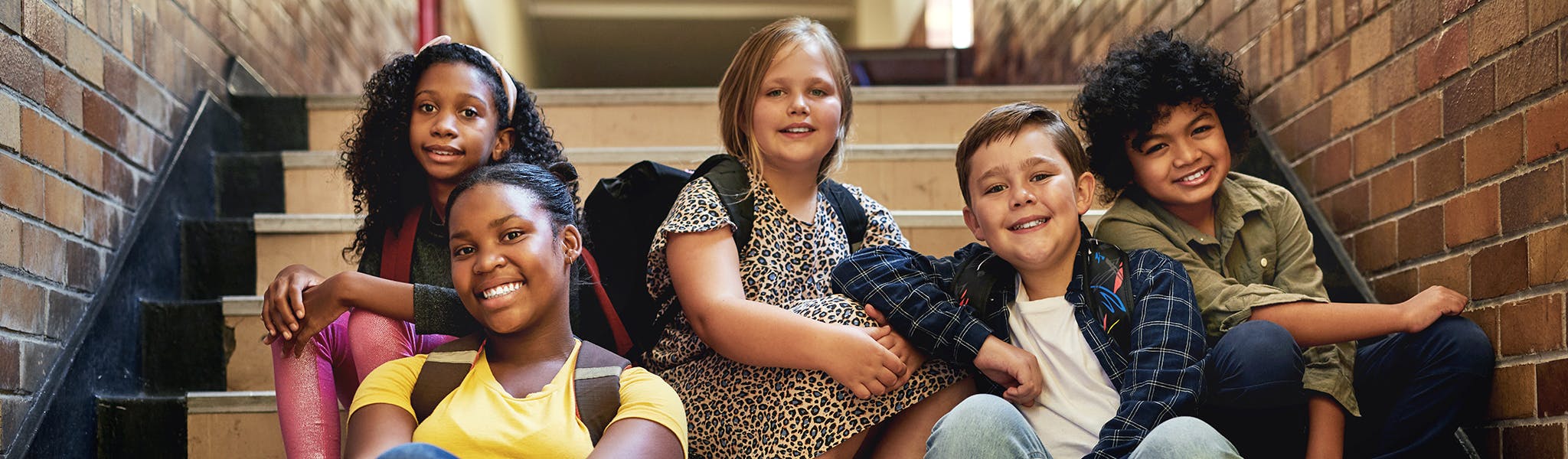 An image of group of diverse children sitting on the stairs in a building