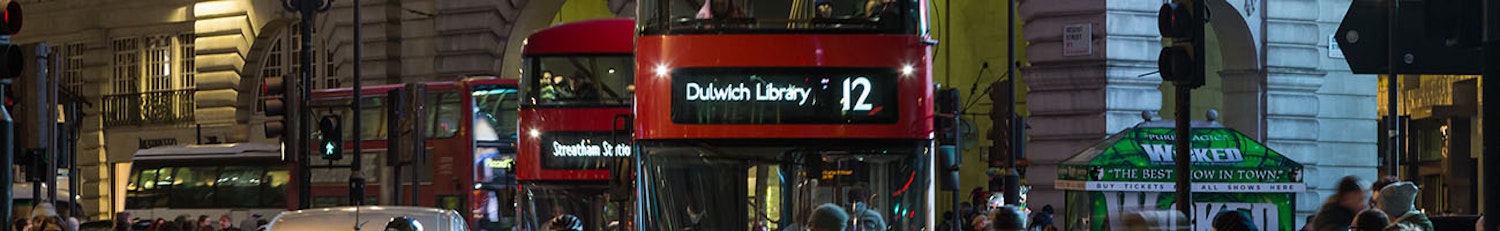 Three red London Buses driving through central London at night