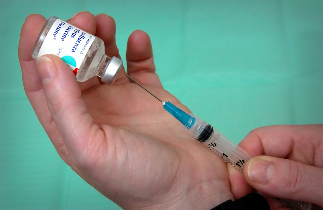 Image of hands holding a needle and flu vaccine