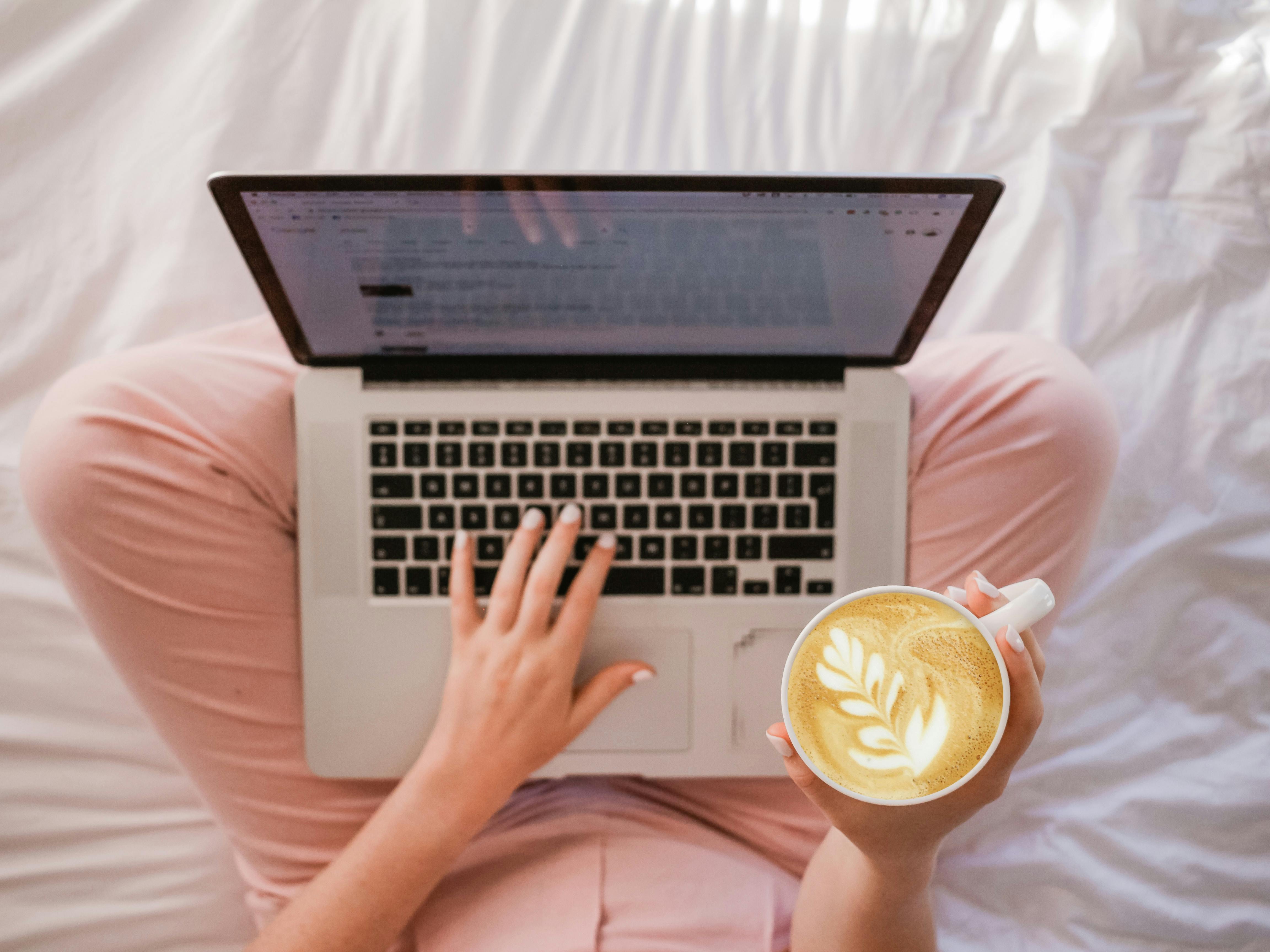 Overhead shot of woman in pink trousers with laptop and coffee writing a blog post