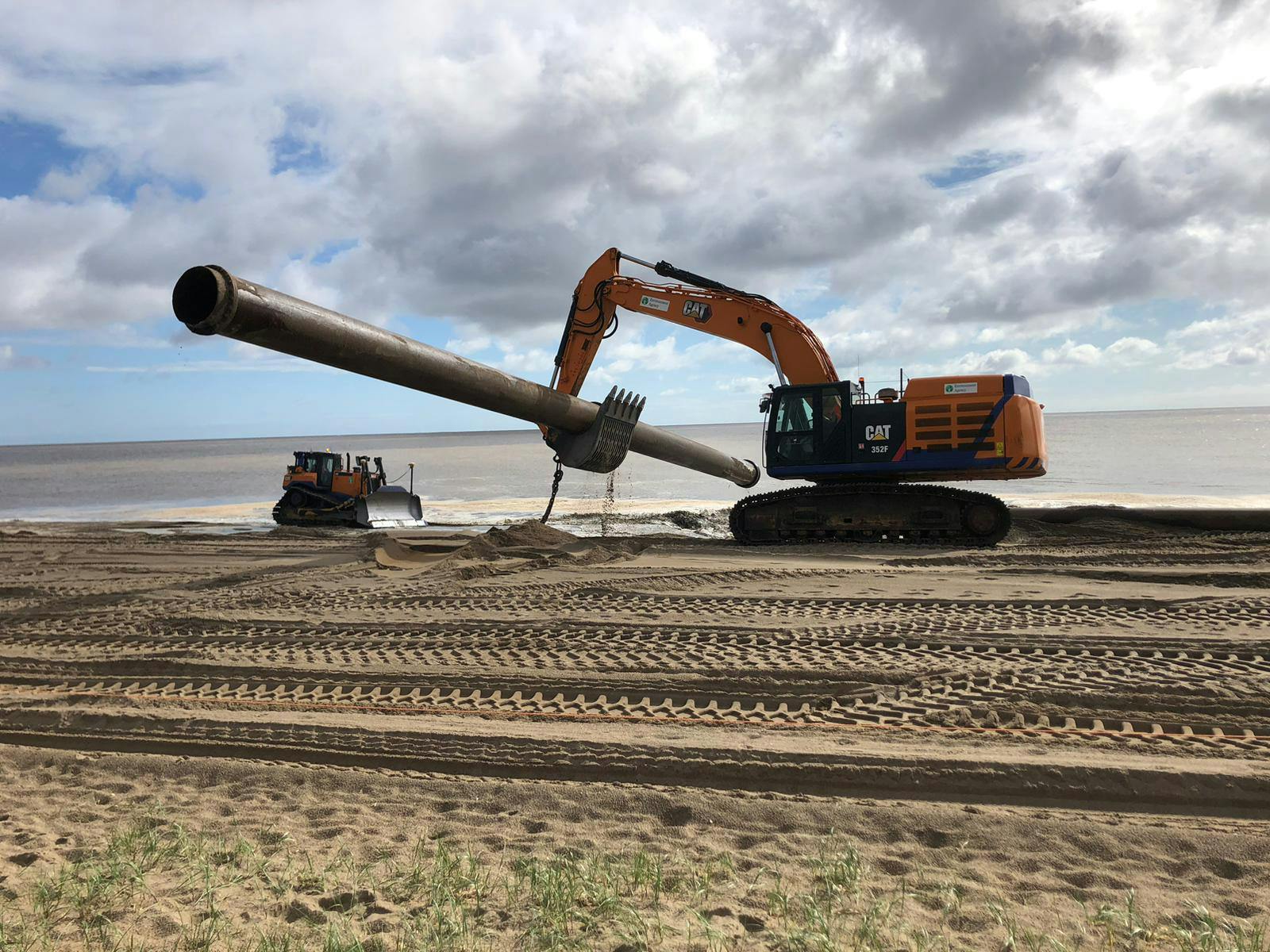 An excavator moves the nourishment pipe on the beach next to the sea
