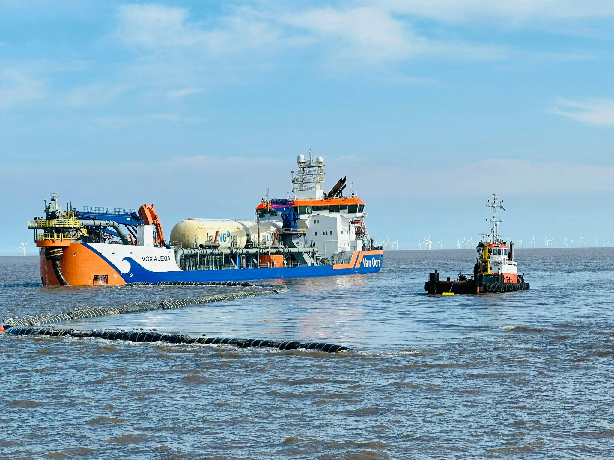 A tug boat moves the sinkerline beside the Van Oord dredger with the Tritton Knoll windfarm on the horizon