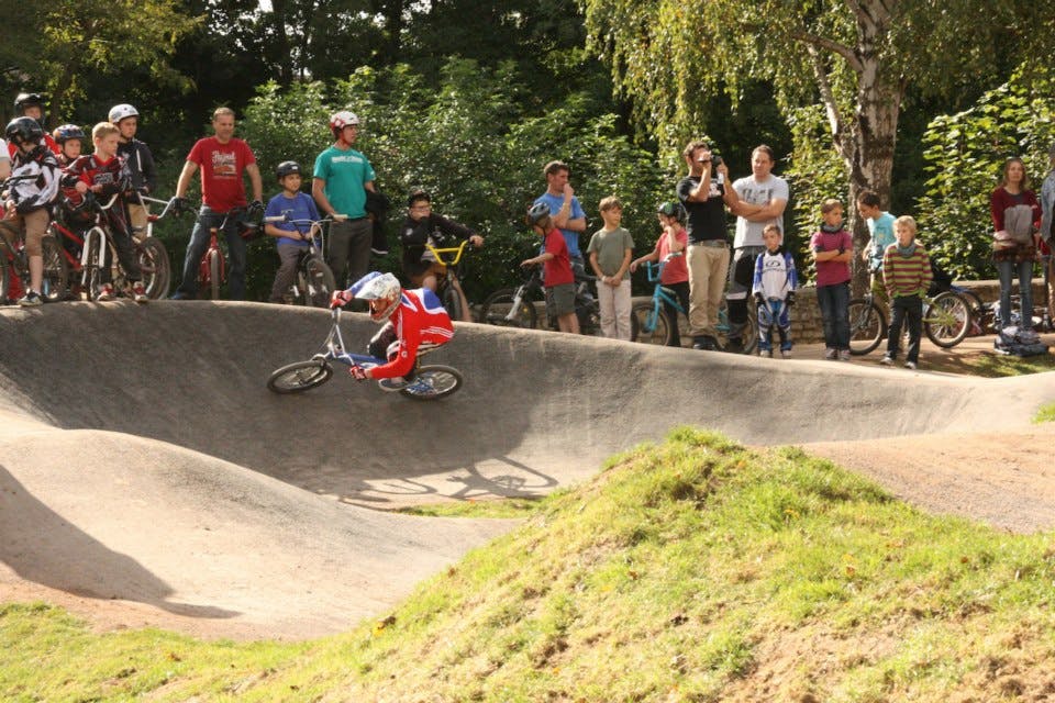 BMX biker using a pump track, watched by bystanders.