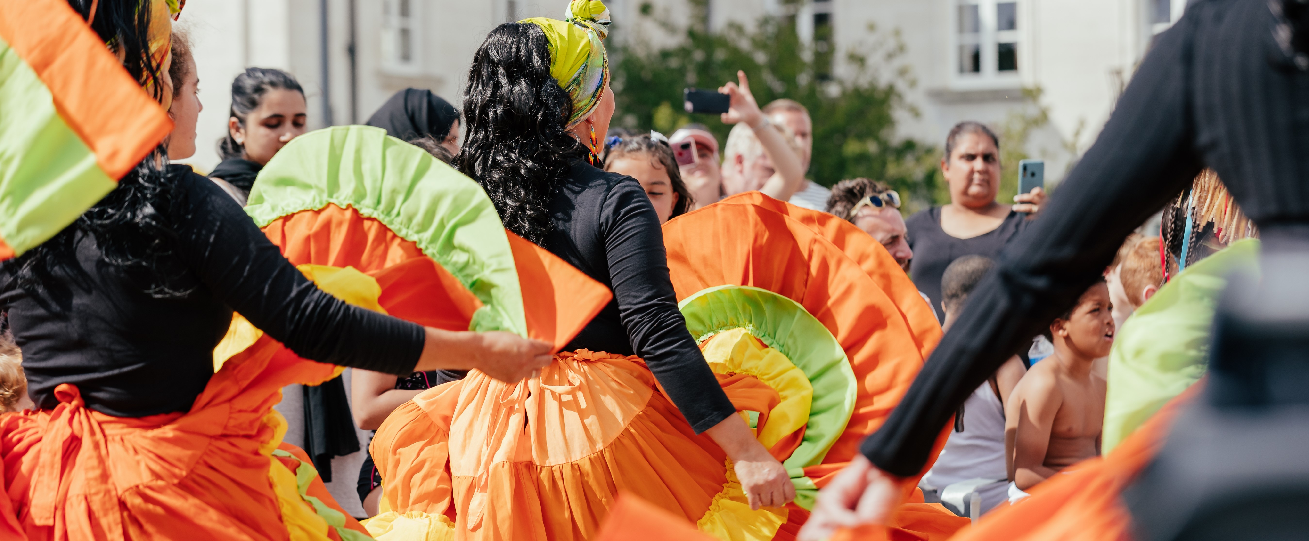 Photograph of women dancing in orange and green skirts at Fellowship Feast. Photograph by Odera Okoye.