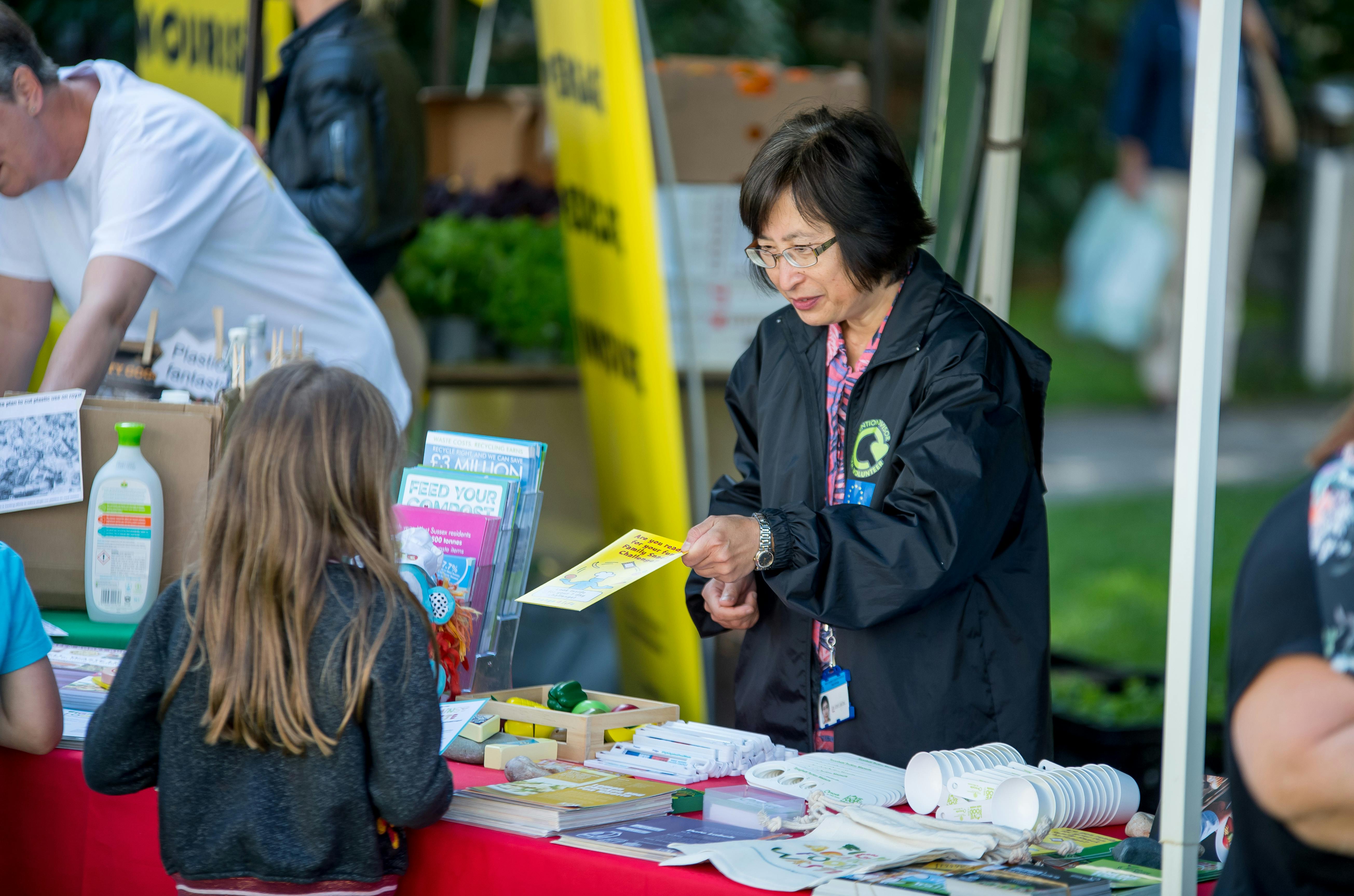 A Waste Prevention volunteer handing out a leaflet to an interested child at an event stand.