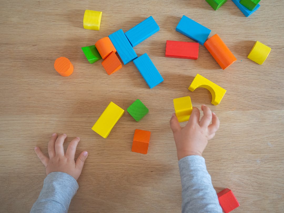 A toddler plays with coloured bricks on a wooden floor