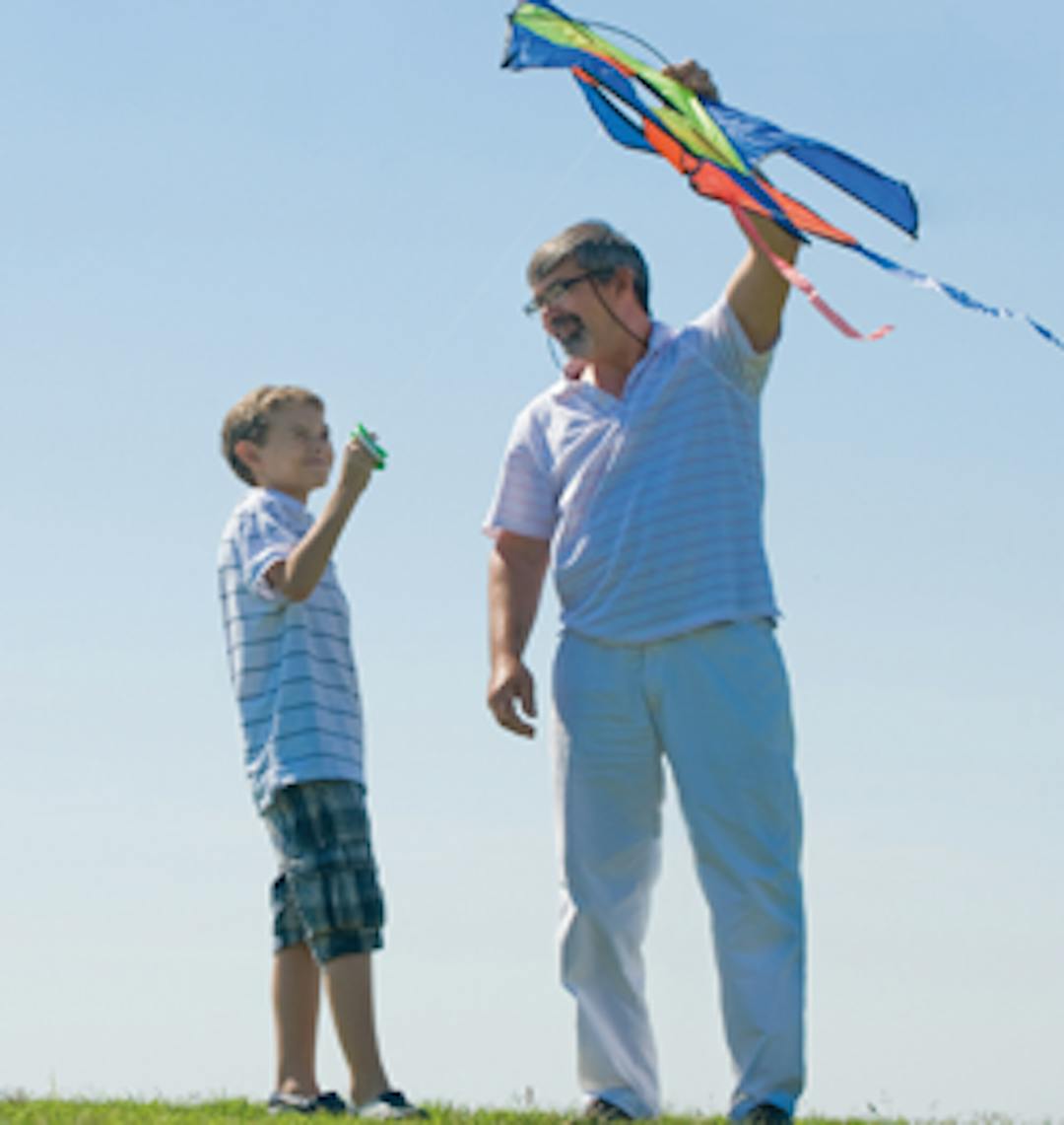 Image shows a male adult and a male child flying a kite together