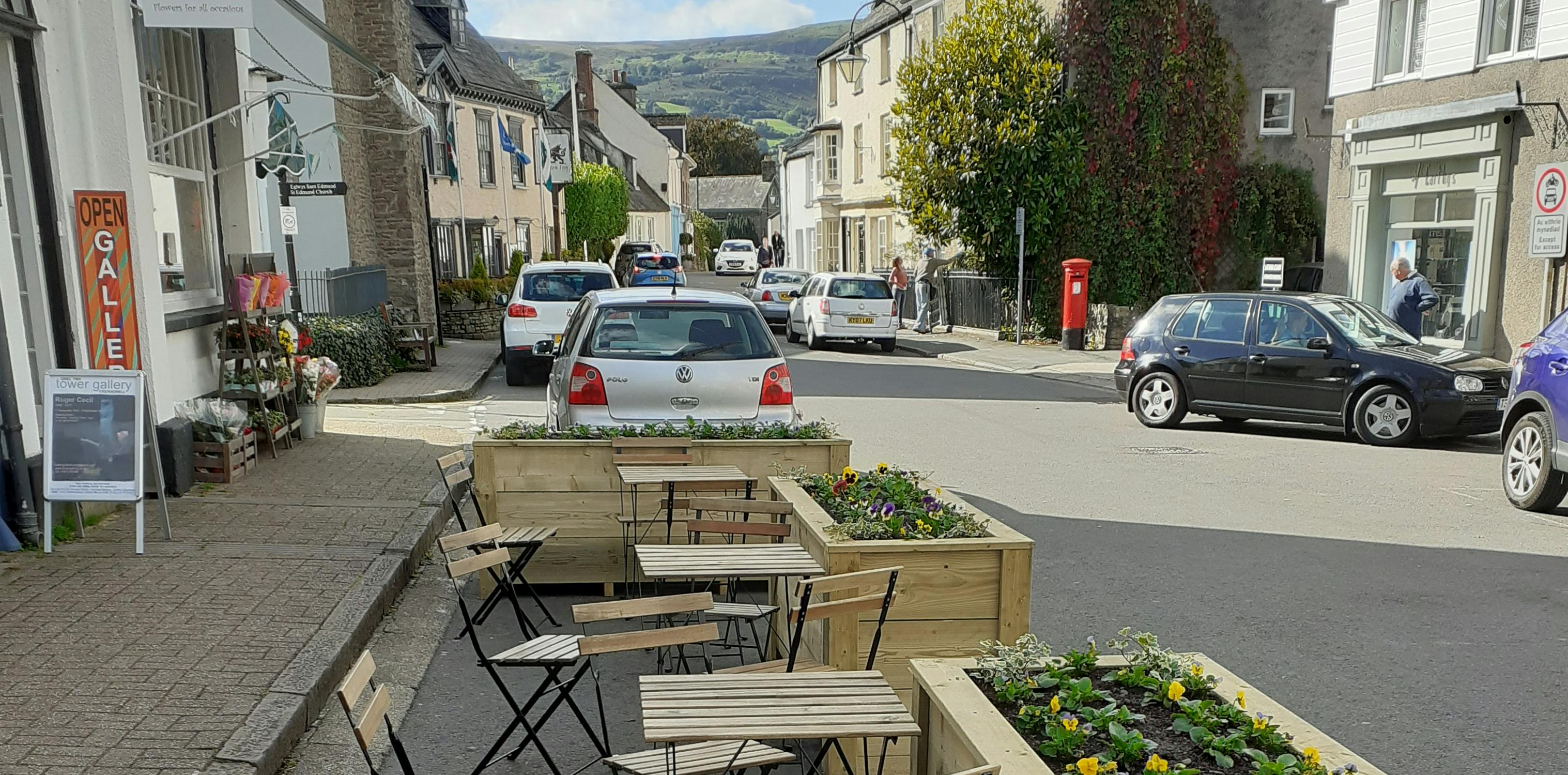 Image of table and chairs outside on the street surrounded by planters.