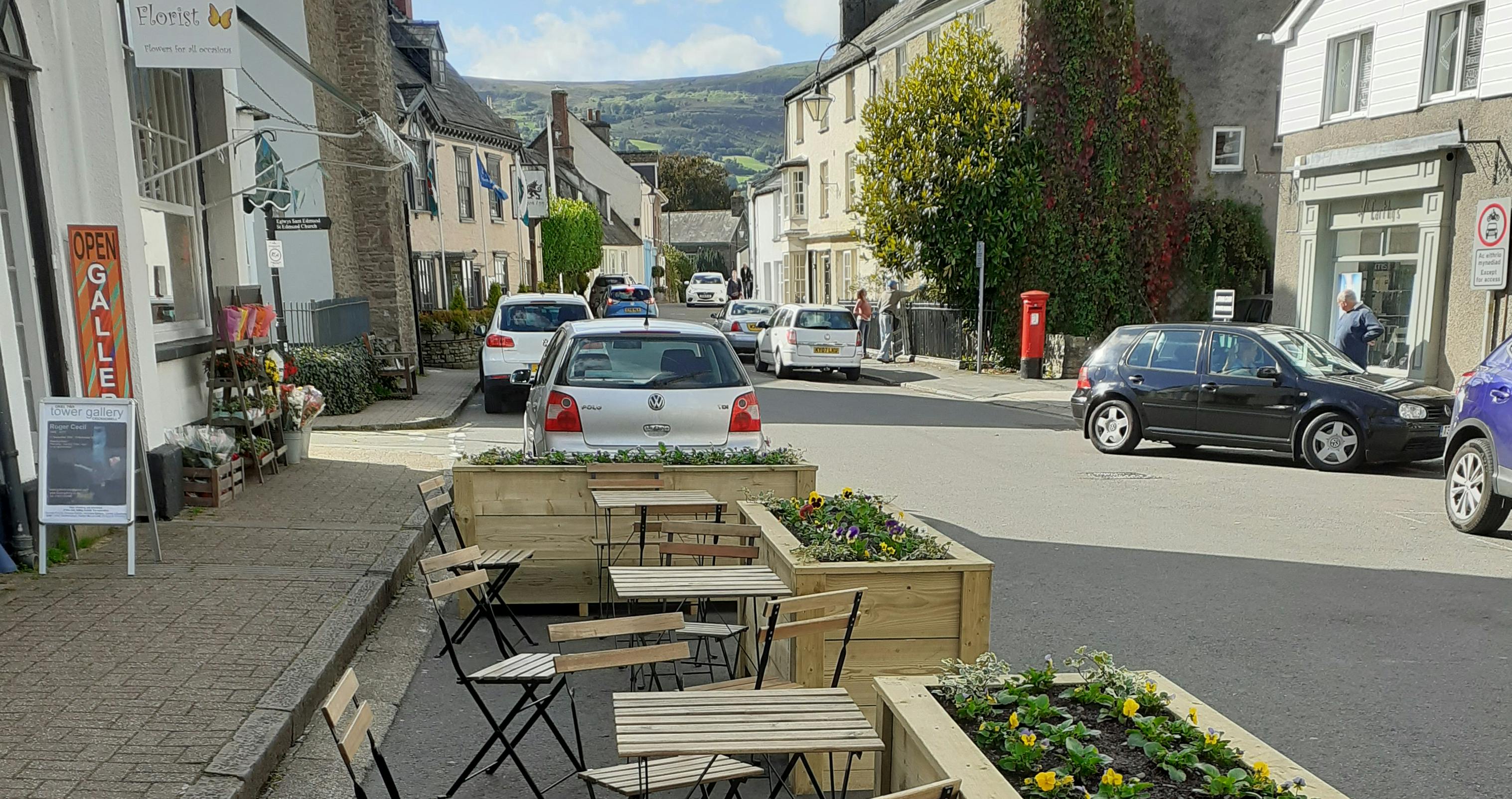 Image of table and chairs outside on the street surrounded by planters.