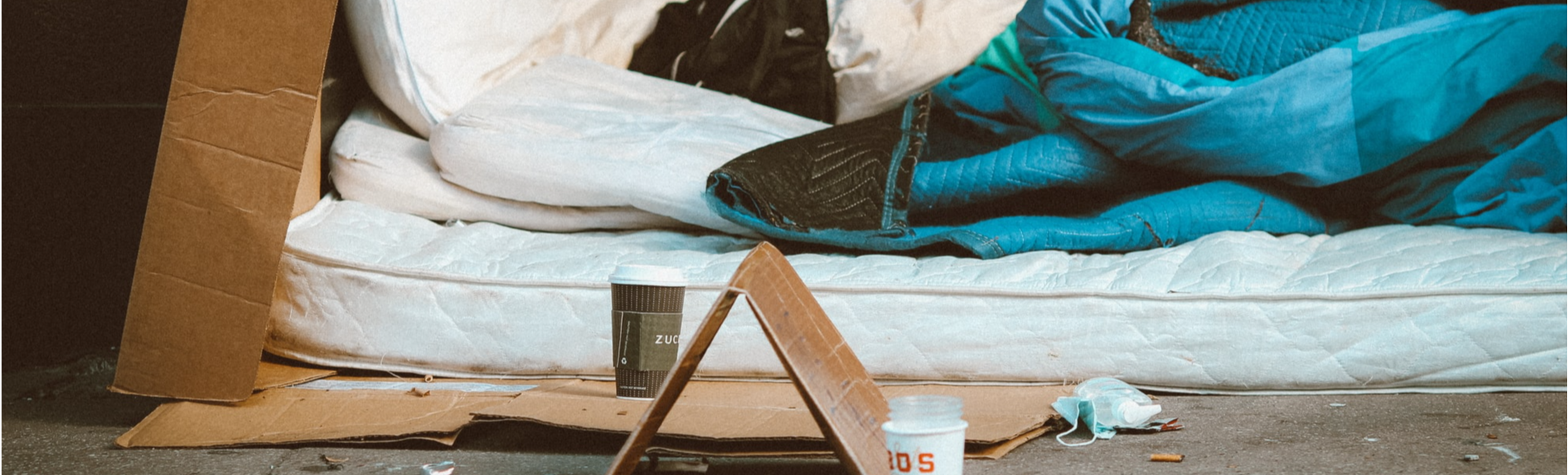 A homeless person's bed on a pavement showing a mattress laid on cardboard with a sleeping bag