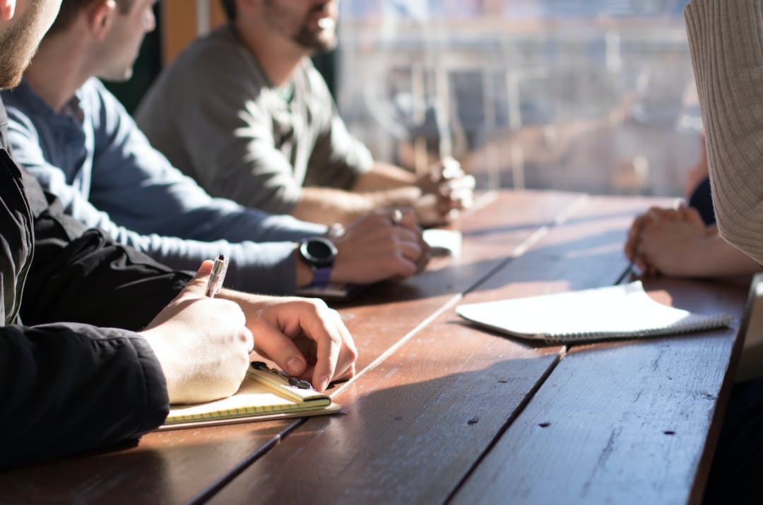 Adults sitting at a sunlit table working together and talking. 