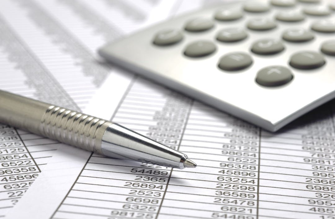 A picture of a pen, spreadsheet and calculator on a desk