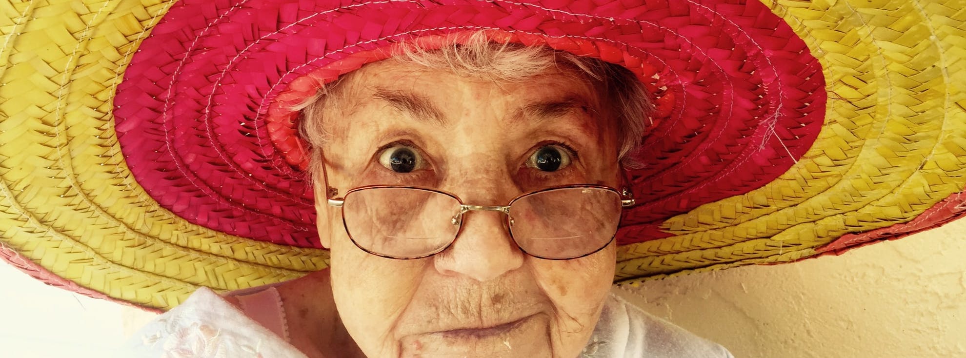 Elderly lady looking directly at the camera wearing a red and yellow sombrero hat.