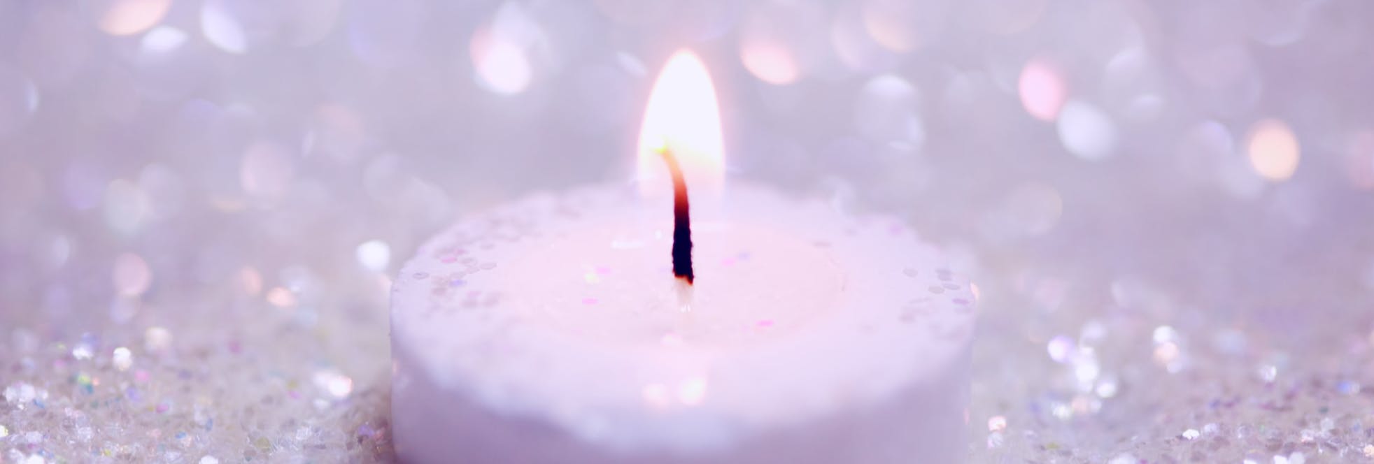 A white tealight candle on a sparkling white background to symbolise remembrance