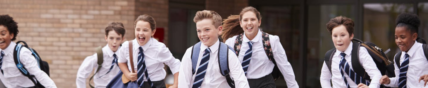 Image of seven happy, smiling school children running across a school yard
