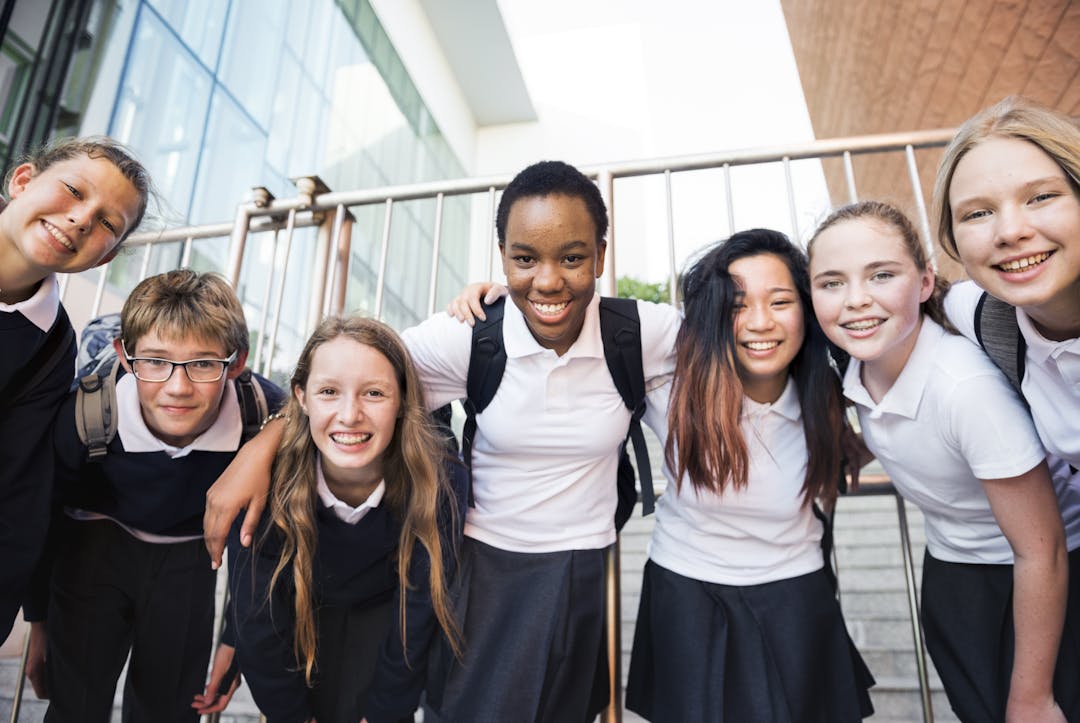 Group of seven school children linking arms and smiling towards the camera