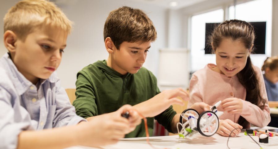 Children (two boys and a girl) working on making things together around a table