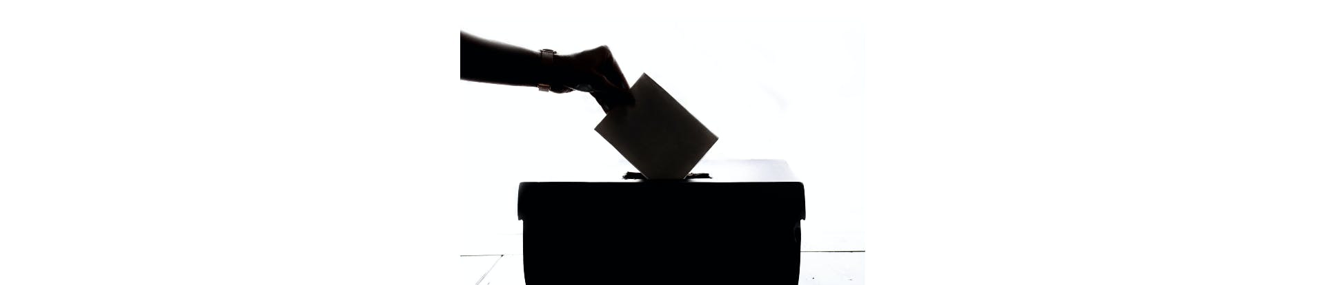 Silhouette of a hand placing a voting slip into a ballot box