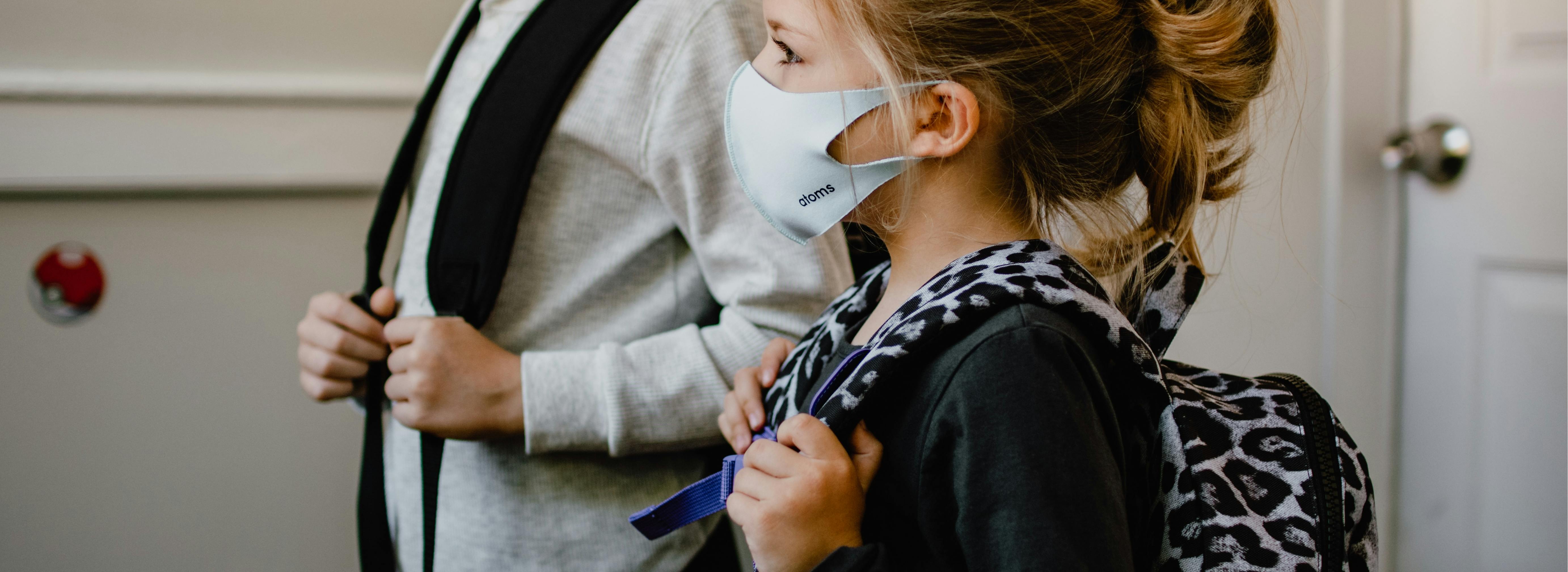 two children with rucksacks and face masks in a classroom